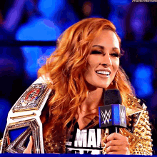 a woman with red hair is holding a wrestling championship belt and a microphone with the letter w on it