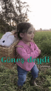 a little girl in a pink shirt is carrying a basket with the word günes deydi written on it