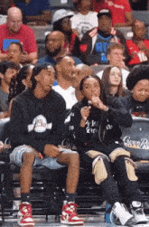 a group of people sitting in the stands at a basketball game with one wearing a black hoodie that says atl