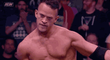 a shirtless wrestler is standing in front of a crowd with aew written on the bottom of his shirt