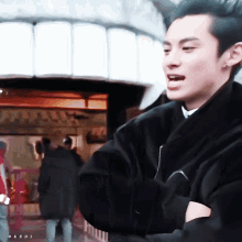 a man in a black coat is standing in front of a building with his arms crossed