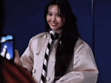 a woman wearing a white jacket and a black and white striped tie smiles for the camera