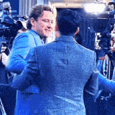 a man in a blue suit is hugging another man in a gray jacket