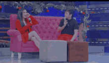 a man and a woman are sitting on a pink couch and talking into microphones