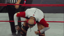 a wrestler is bending over in a wrestling ring with a referee standing behind him