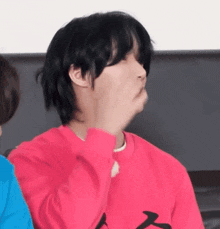 a young man with black hair is wearing a red sweater and making a funny face .