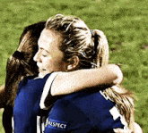 two female soccer players are hugging each other and one has a respect patch on her jersey