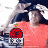 a man wearing a red shirt and a black hat with a logo for osasco volleyball club on it