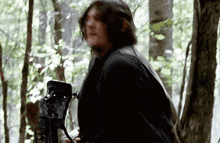 a man is standing in the woods holding a camera .