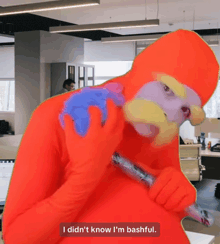 a man in an orange costume is holding a game controller and says i did n't know i 'm bashful