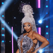 a drag queen with white dreadlocks and a silver dress on a stage