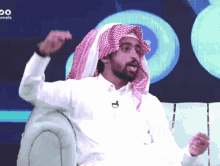 a man in a white shirt and a head scarf is sitting in front of a sign that says channels