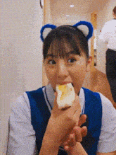 a young girl wearing a headband with ears is eating a piece of food .