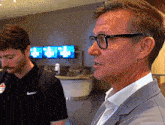 a man wearing glasses stands next to another man in a black nike shirt