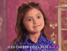 a little girl in a blue shirt is making a face and saying iced cherry chia latte .