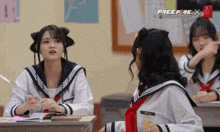 three girls in school uniforms are sitting at desks in front of a screen that says freefire