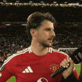 a man in a red manchester united shirt is holding a microphone