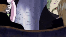 a group of people are sitting in a dark room and one of them has a pink scarf around his neck