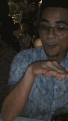 a man wearing glasses is covering his mouth with his hand in a dark room