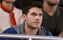 a man in a blue jacket sits in the stands watching a baseball game