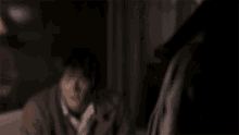 a blurry picture of a man in a suit talking to another man in a dark room .