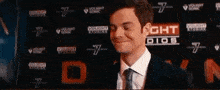 a man in a suit and tie is standing in front of a wall with a lot of logos on it