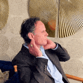 a man in a suit is sitting in a chair with his hands on his neck