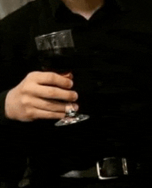 a man in a black shirt is holding a glass of wine in his hand .