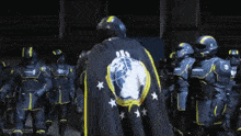 a group of soldiers are standing in a line with one wearing a black cape with a globe and stars on it