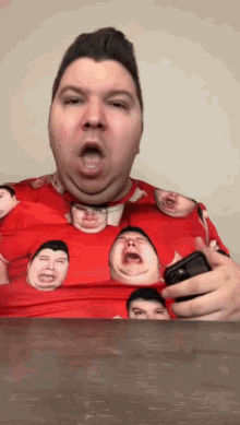 a man wearing a red shirt with faces on it is holding a cell phone