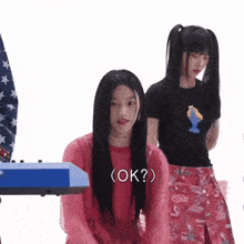 a girl in a red sweater says ok while another girl stands behind her