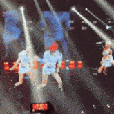 a group of women are dancing on a stage with a cell phone taking a picture of them
