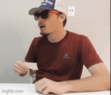 a man wearing a hat and sunglasses is sitting at a table with a card in his hand ..