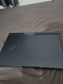 a black laptop is laying on a bed with a brown blanket