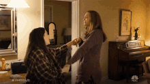 two women holding hands in a living room with a nbc logo on the bottom