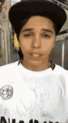 a young man wearing a black hat and a white shirt is making a funny face .