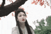 a woman standing under a tree with red flowers on it