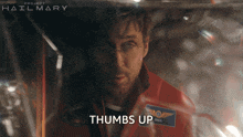 a man in a red jacket says thumbs up in front of a project hailmary poster