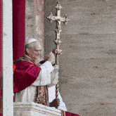 a man in a red robe holds a cross in his hand