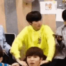 a group of people are sitting in a room and one of them is wearing a yellow sweatshirt .
