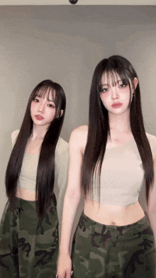 two girls with long hair are standing next to each other wearing camouflage pants