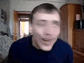 a man in a blue sweater is sitting on a couch in a living room making a funny face .
