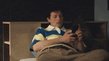 a man wearing a blue and yellow striped shirt is laying on a bed looking at his phone