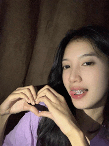 a girl with braces on her teeth making a heart shape with her hands