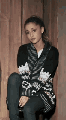 a woman wearing a black and white sweater sits on a wooden stool