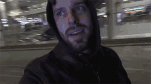 a man with a beard is wearing a black hooded jacket