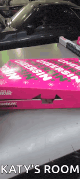 a pink box of dunkin donuts sits on a table next to a car ..