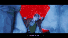 a woman in a green top is surrounded by giant heads and the words tse nine on fire are visible