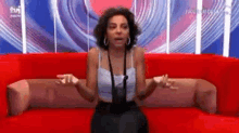 a woman is sitting on a red couch with her arms outstretched and talking .