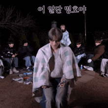 a man wrapped in a blanket stands in front of a group of people with korean writing on the bottom